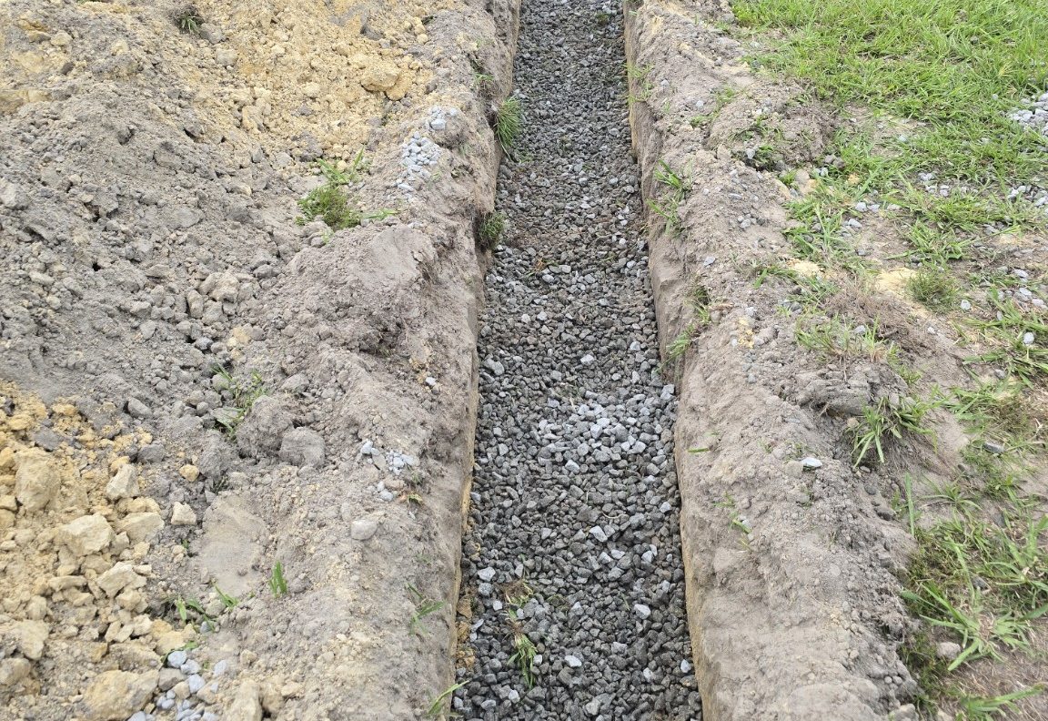 Excavated drainage trench with aggregate bedding for site drainage work